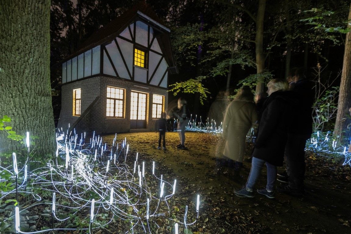 A lit cottage in the woods, with visitors on the route